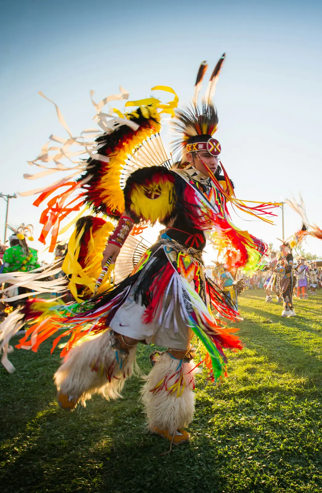 A dancer in full regalia at a powwow, mid-step on green grass